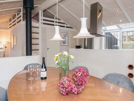 A dining area with a wooden table, white pendant lights, a bottle of wine, and a vase of flowers.