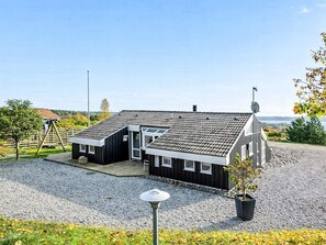 A two-story building with a gravel driveway and a fenced area. - 4 Star Holiday Home in Ebeltoft (Ebeltoft)