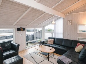 A modern living room with a sofa, armchair, and coffee table, large windows, and a ceiling with exposed beams. - 4 Star Holiday Home in Ebeltoft (Ebeltoft)