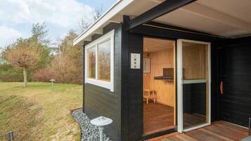 Un edificio moderno con una terraza de madera, puerta de cristal de entrada y un pequeño espacio de estar al aire libre.