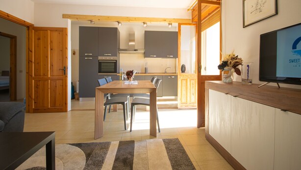 A modern kitchen with grey cabinets, a wooden dining table, and a TV on a wooden stand. - Berchida 6 - Two Bedroom Apartment, Sleeps 5 (La Caletta)