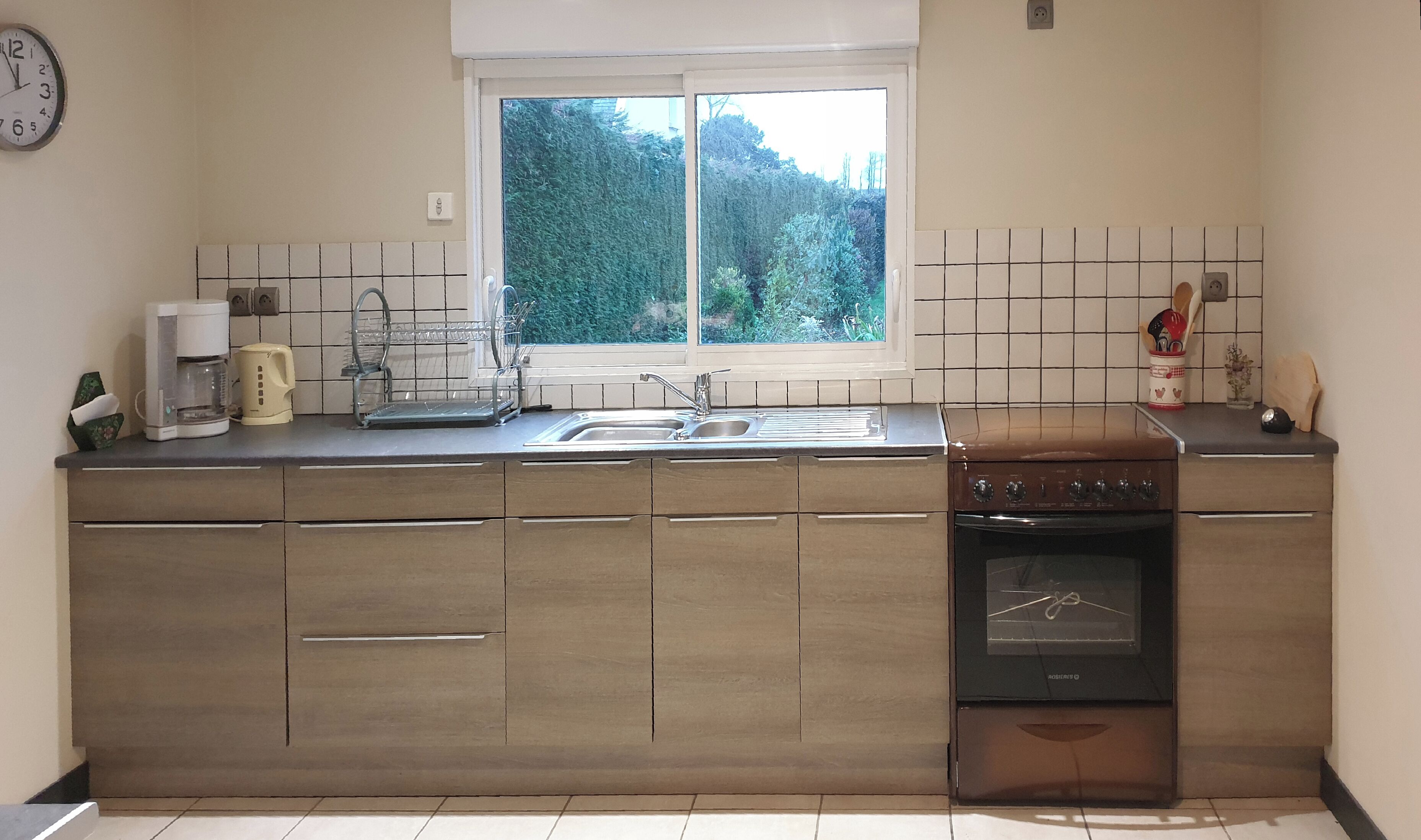 Eine kleine Küche mit Fenster, einer Kaffeemaschine, einem Spülbecken und einem Herd.