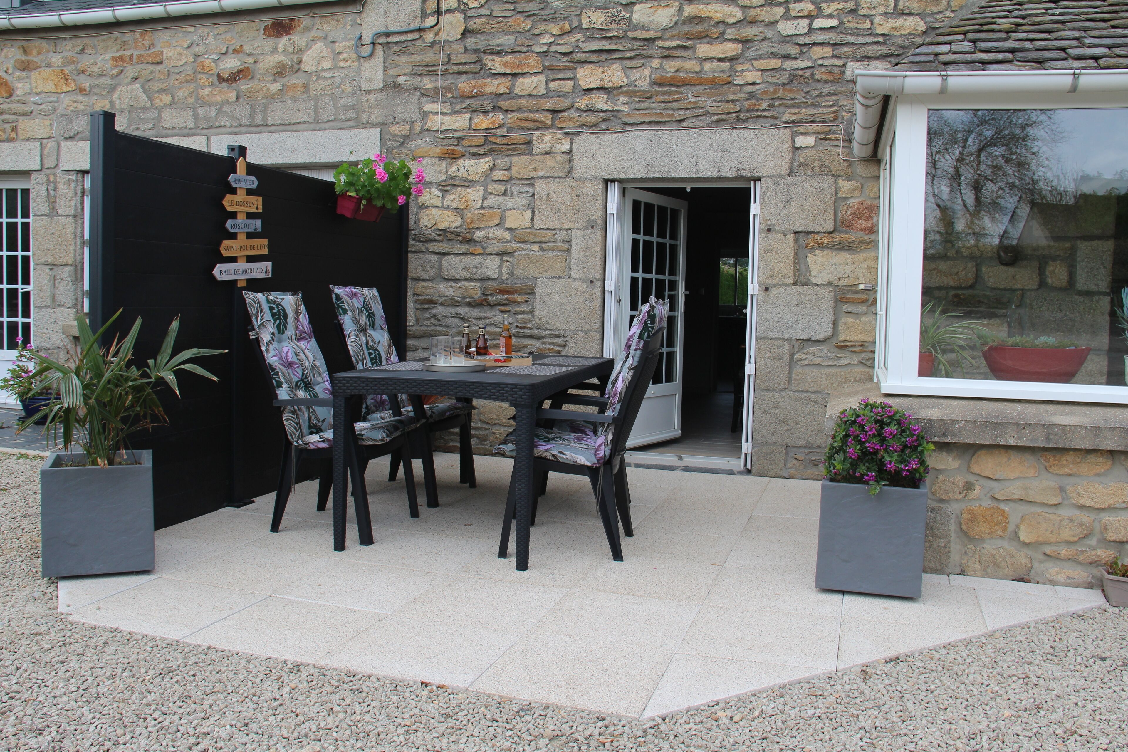Une terrasse extérieure avec une table et des chaises, entourée de murs en pierre et de plantes en pot.