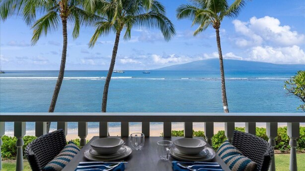 Una mesa de comedor con sillas y vista al océano con palmeras.
