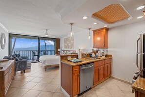 A modern kitchen with wooden cabinets, a dishwasher, and a large window overlooking a balcony. - Beachfront Lahaina Shores 203 | Direct Oceanfront Studio (Lahaina)