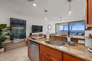 A modern kitchen with granite countertops, stainless steel sink, and a large window overlooking the ocean. - Beachfront Lahaina Shores 203 | Direct Oceanfront Studio (Lahaina)