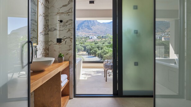 Un baño moderno con un lavamanos grande, un espejo y vistas a un balcón con mobiliario exterior.