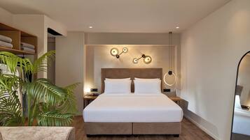 Quarto de hotel moderno com uma cama grande, cabeceira de madeira, luminária fixada na parede e uma planta em vaso.