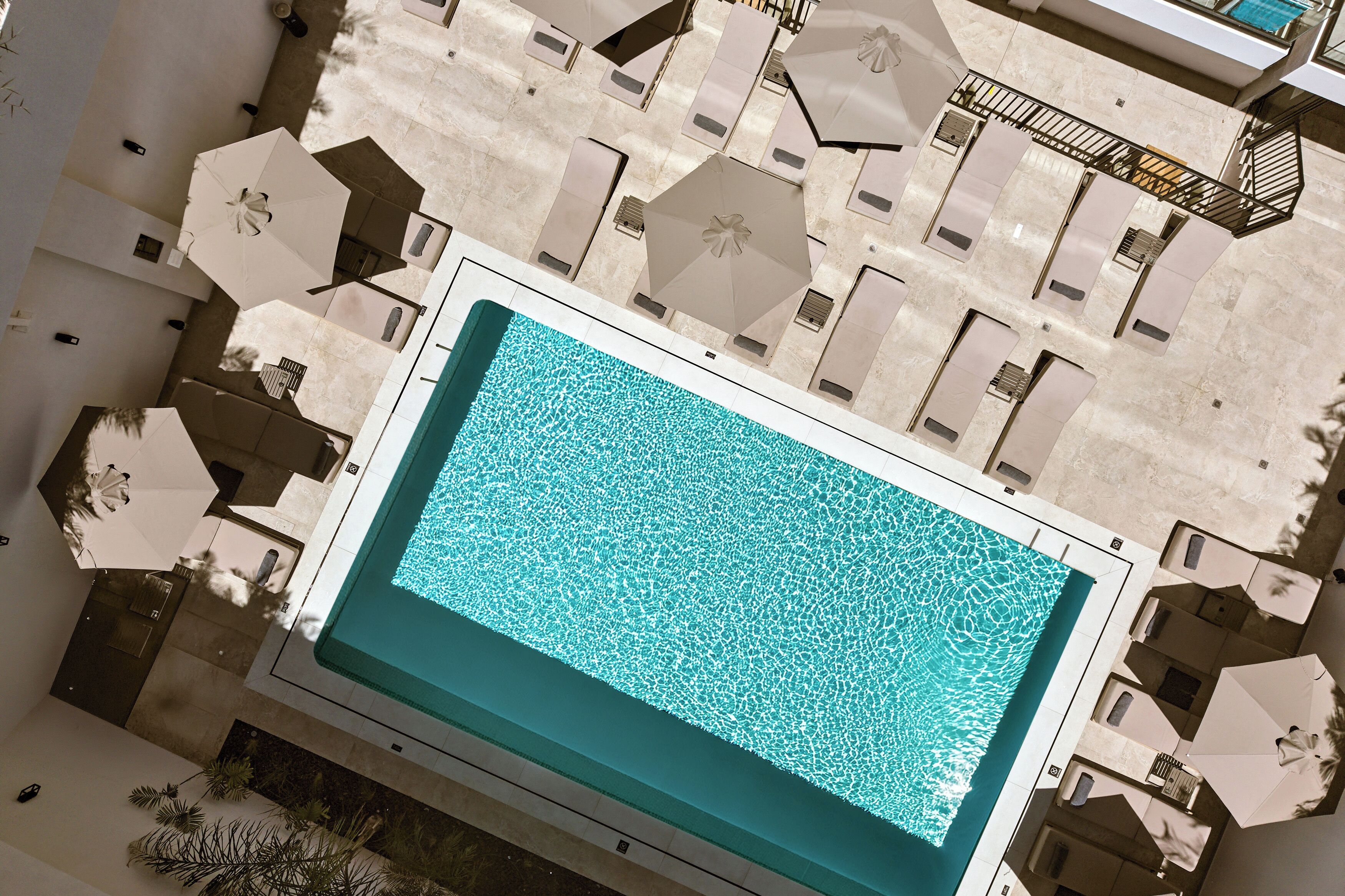A swimming pool with a tiled deck surrounding it, multiple lounge chairs, and umbrellas.