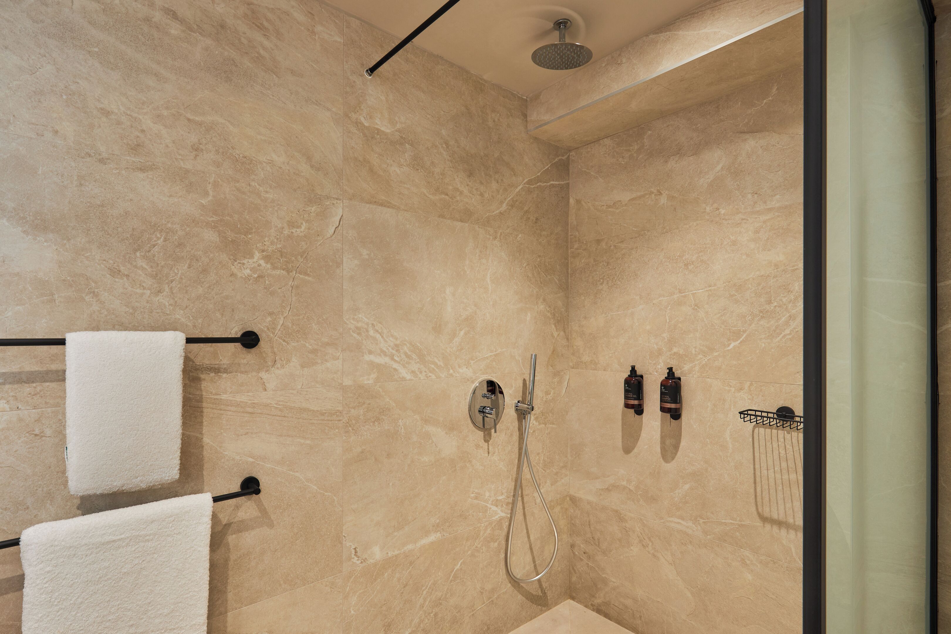 A shower with a handheld showerhead, a wall-mounted faucet, and a towel rack with two towels.