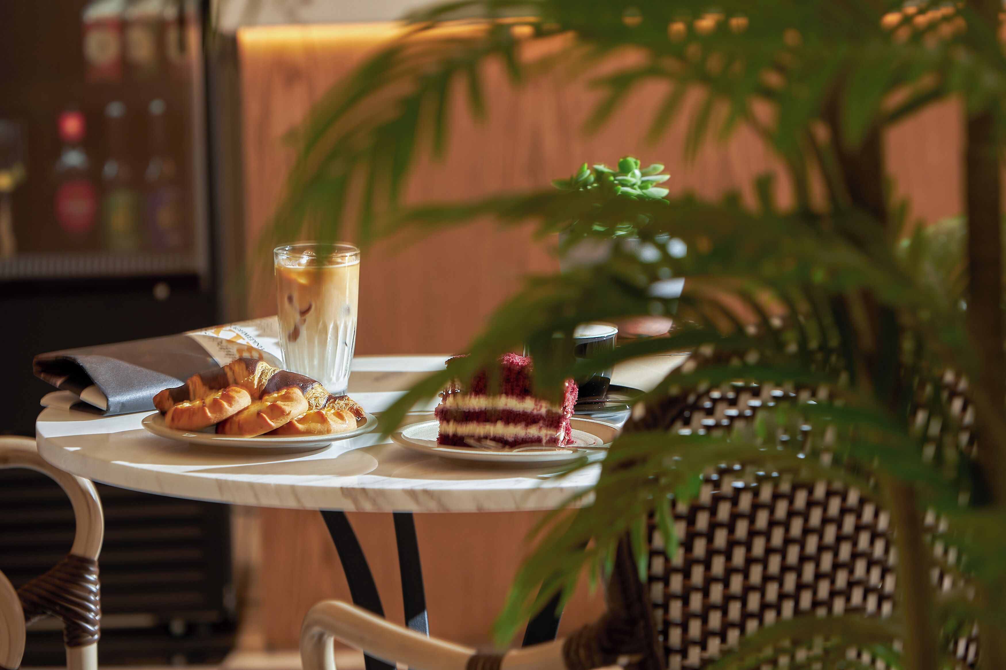 Une table avec des pâtisseries, un verre d’une boisson et une part de gâteau, entourée de chaises et d’une plante en pot.