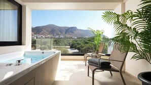Un balcón con jacuzzi, una silla y vistas a montañas y vegetación.