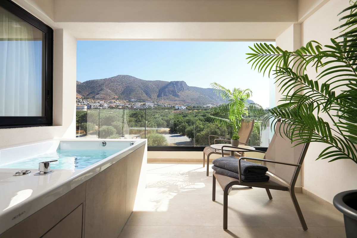 Un balcón con jacuzzi, una silla y vistas a montañas y vegetación.