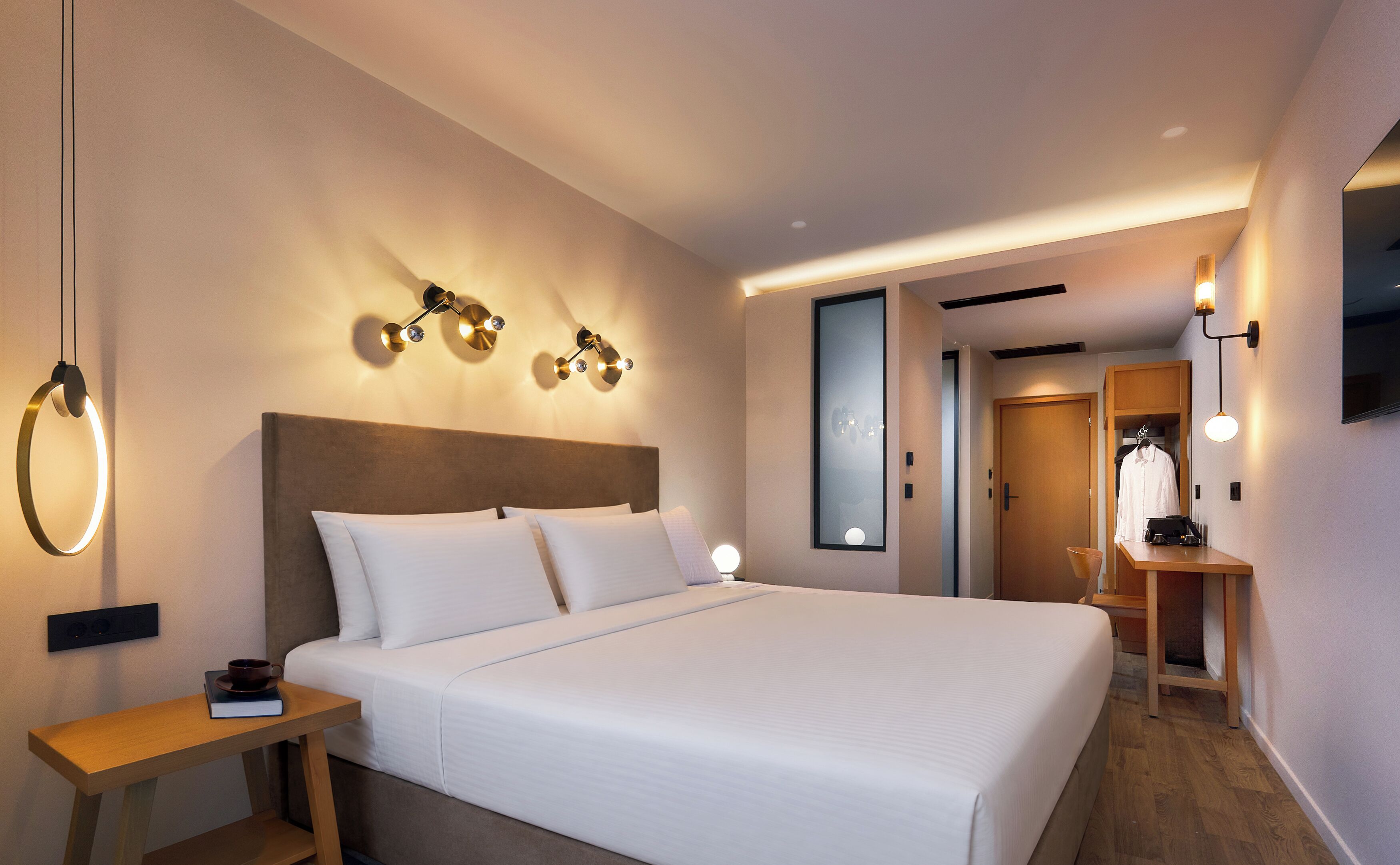A modern hotel room with a large bed, bedside tables, wall-mounted lighting, and a wardrobe.