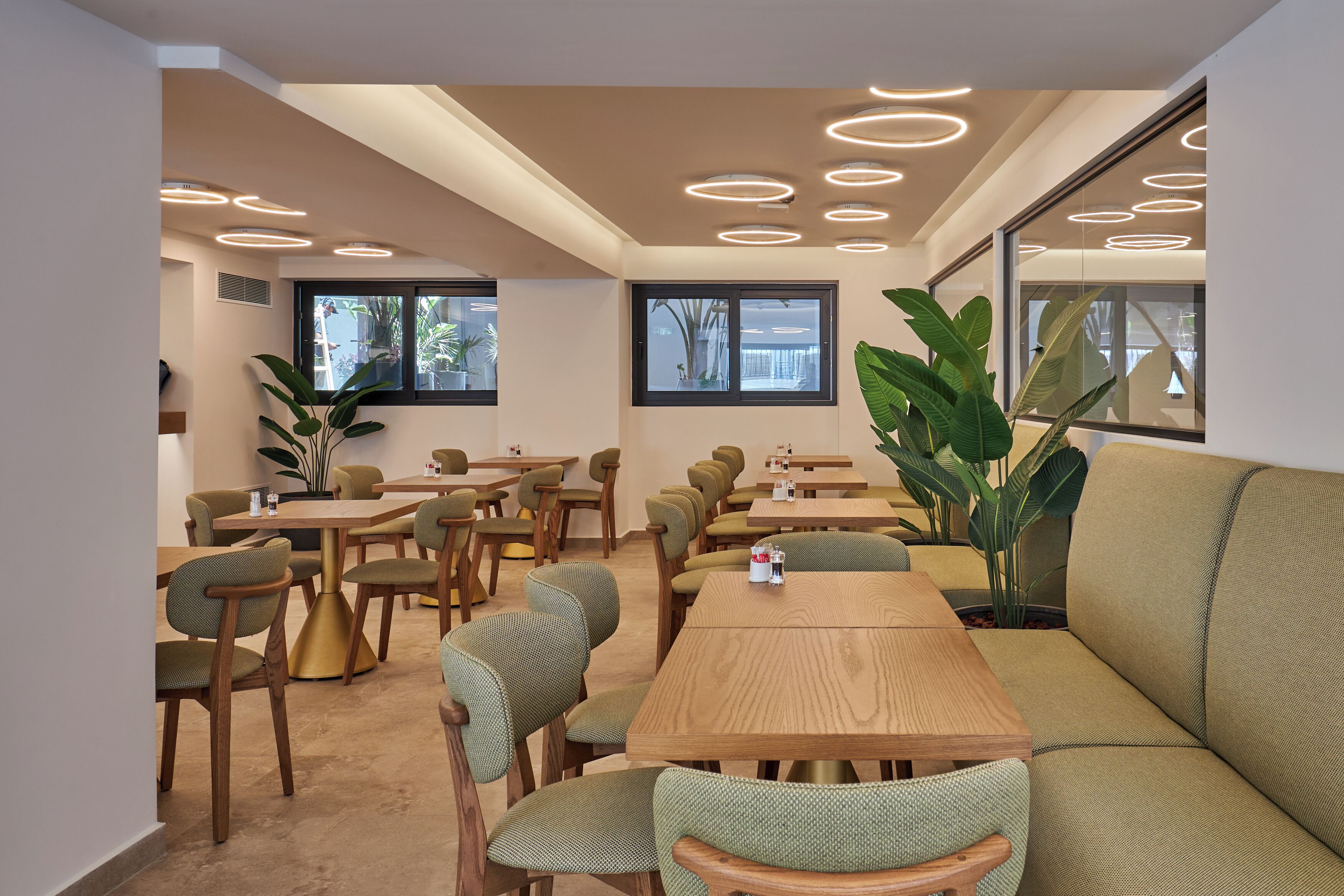 Un comedor moderno con mesas redondas, sillas tapizadas de verde y ventanas amplias.