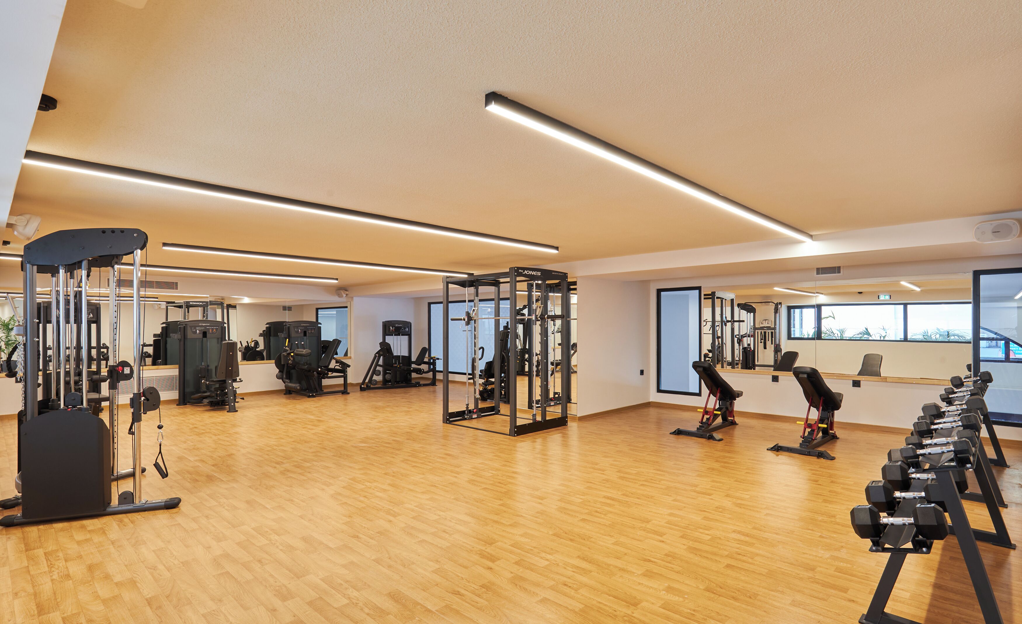 A gym with various exercise equipment, wooden flooring, and large windows.