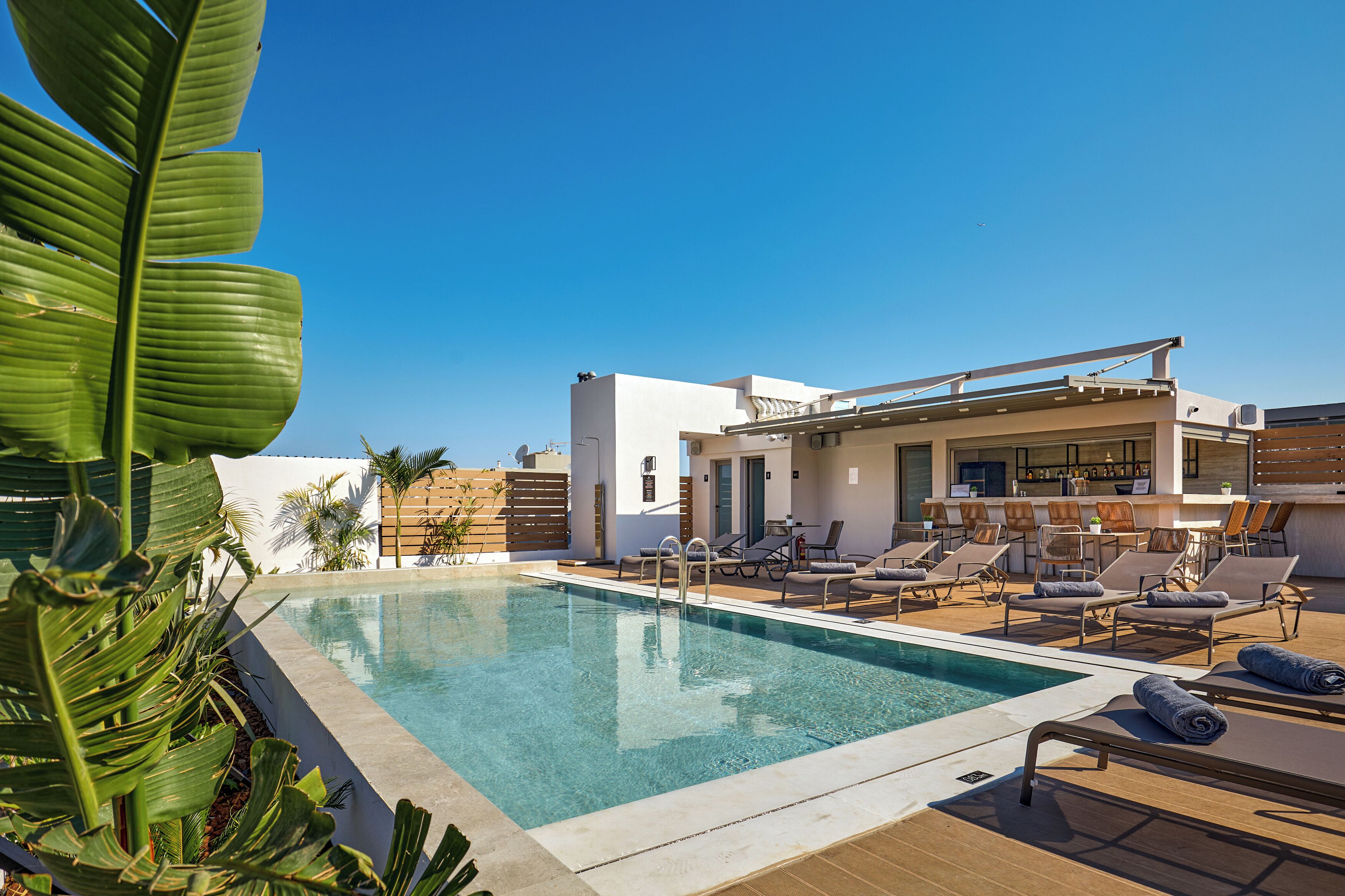 A rooftop pool with lounge chairs, a bar, and a modern building with a flat roof.