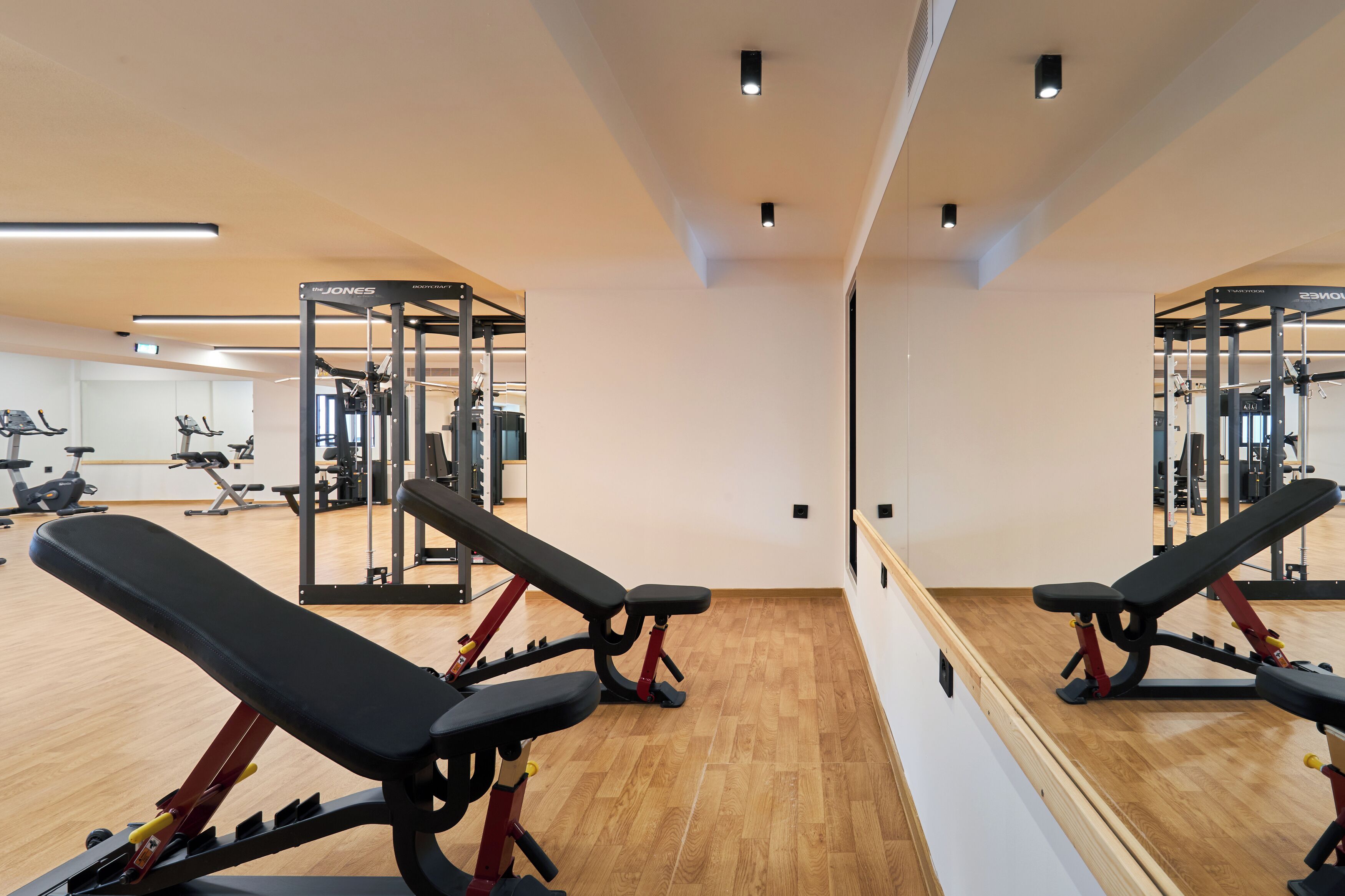 A gym with exercise equipment, wooden flooring, and a large mirror.
