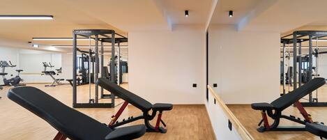A gym with exercise equipment, wooden flooring, and a large mirror.