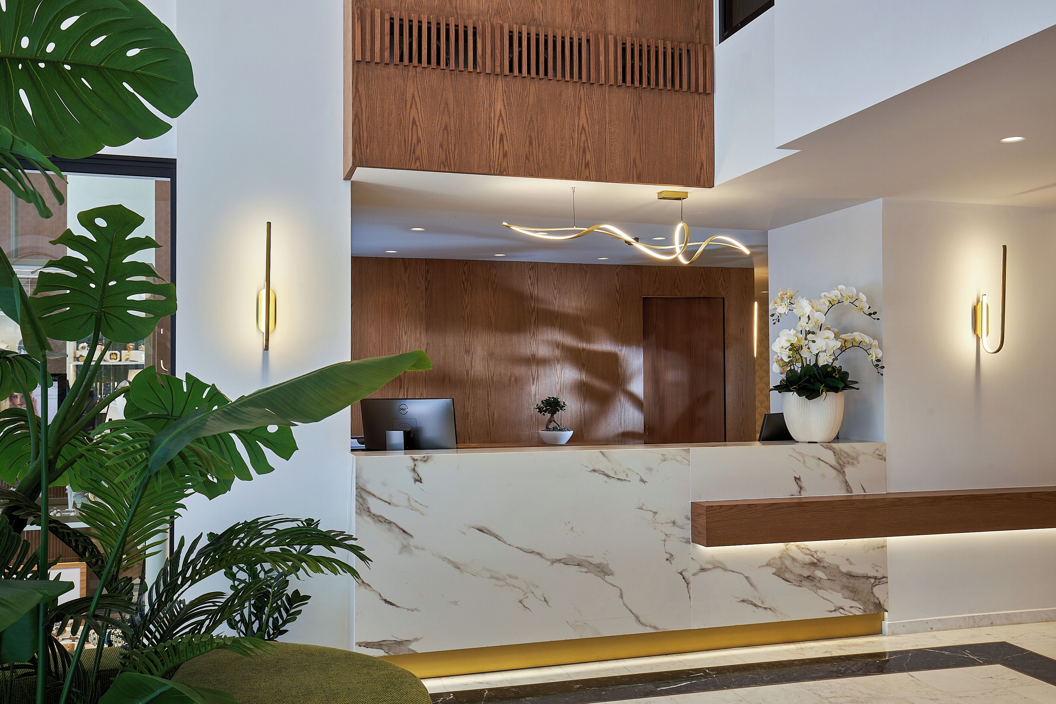 A reception desk with a marble countertop, wooden paneling, and a potted plant.