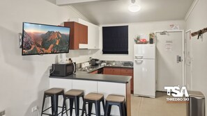 A compact kitchen with a flat-screen TV, a refrigerator, a microwave, and a sink. There are four stools at the counter. - Karas 6 - Central Village (Central Village)