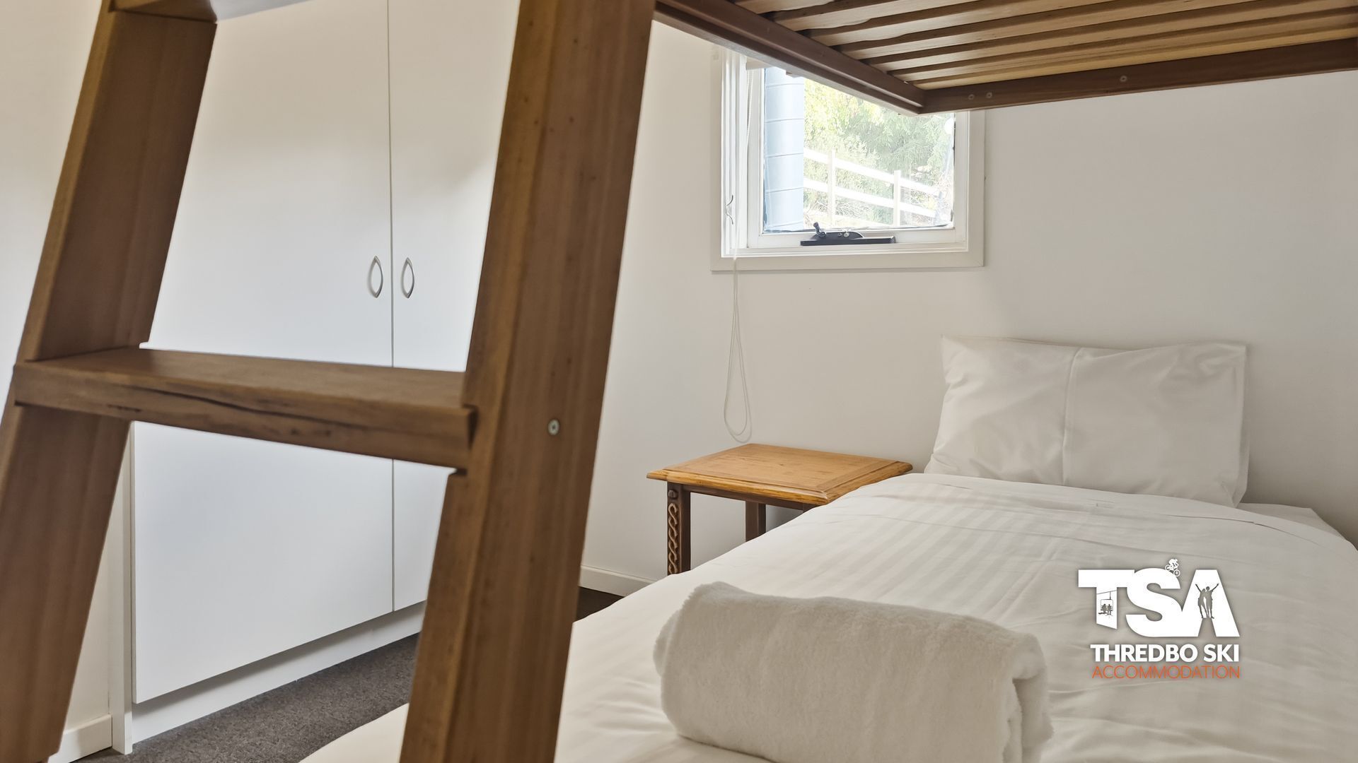 Un dormitorio con cama, una escalera de madera, una mesita y un armario.