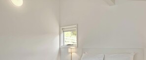 A bedroom with a bed, a nightstand, a lamp, and a window. - Karas 6 - Central Village (Central Village)