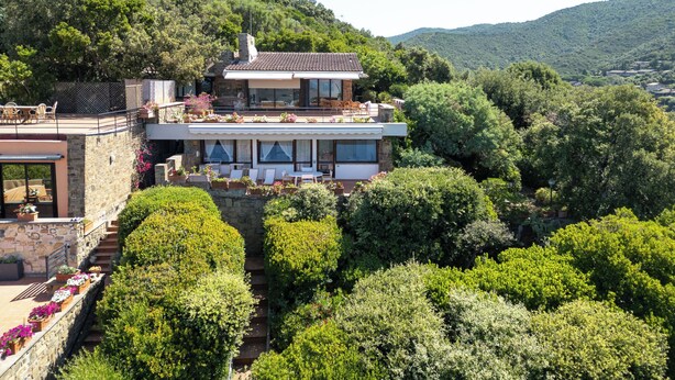 Une maison moderne à deux étages, dotée d’une façade en pierre, de grandes fenêtres et d’une terrasse sur le toit.
