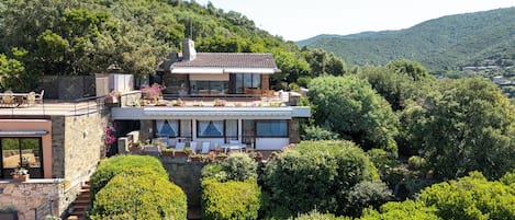 Una casa moderna de dos pisos con fachada de piedra, ventanas amplias y una terraza en la azotea.