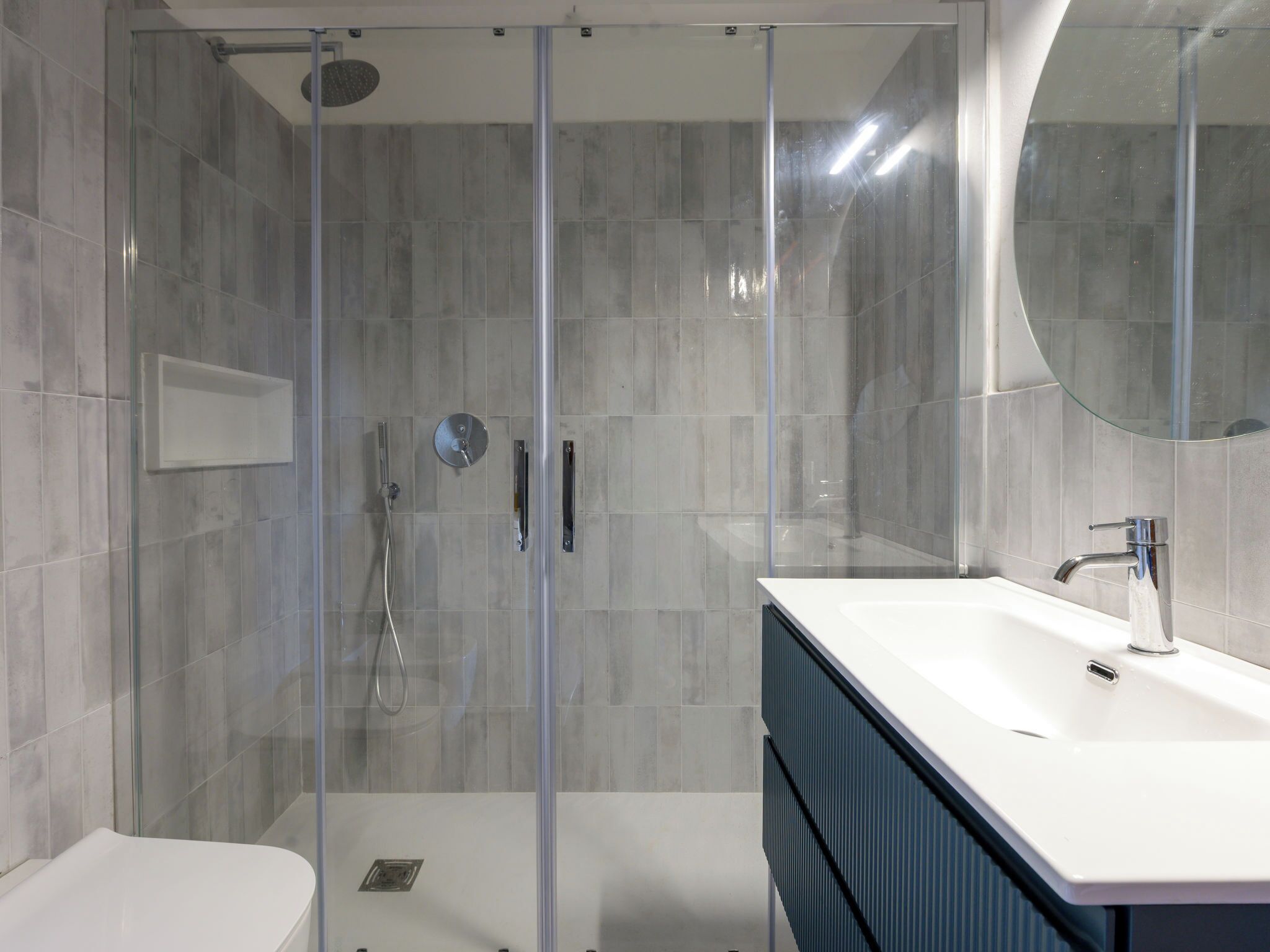 A modern bathroom with a glass-enclosed shower, a white sink, and a large mirror.