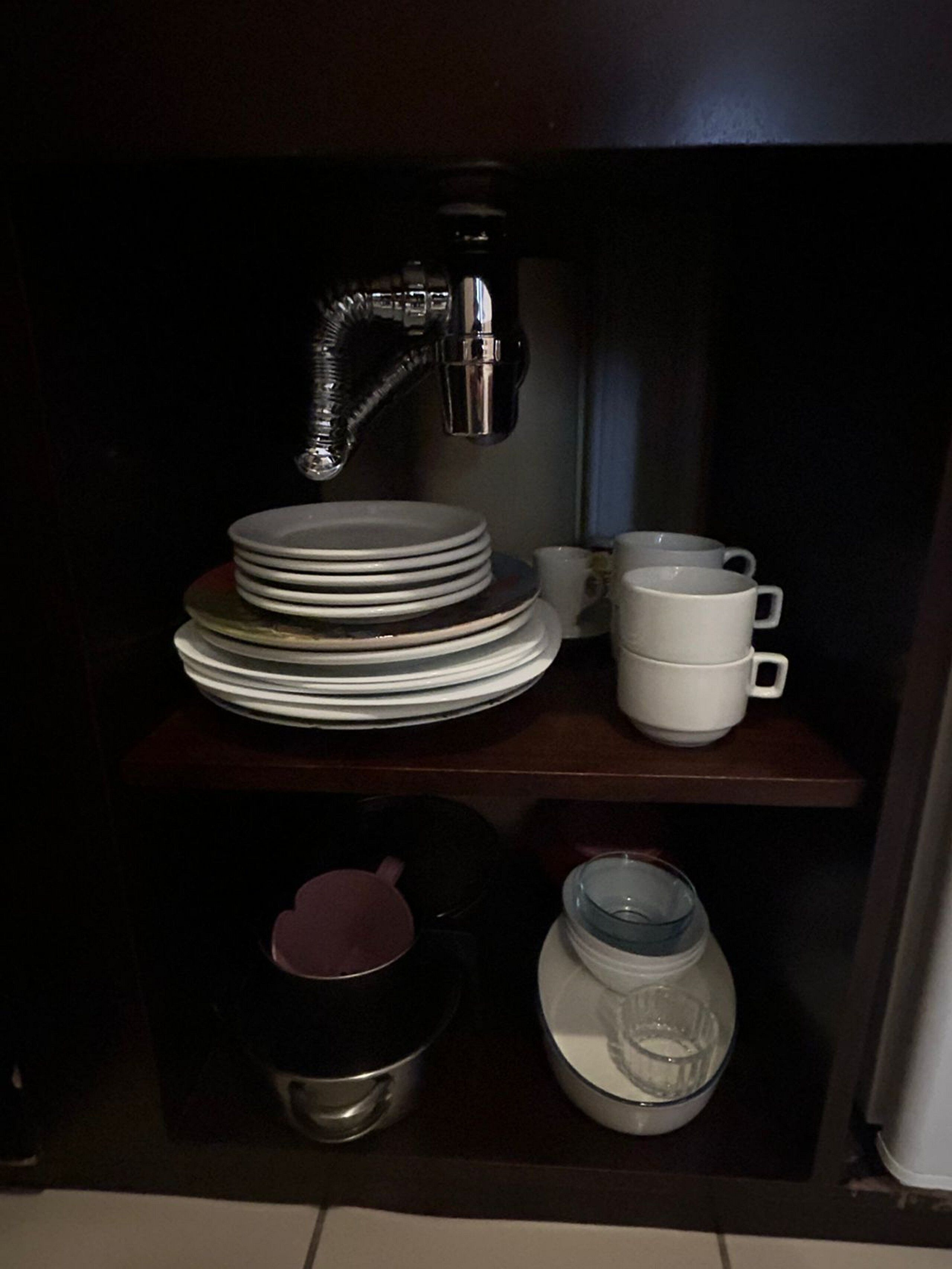 Een spoelbak met een stapel borden en bekers, een zwarte pan, en een glazen pot.