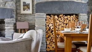Una chimenea de piedra con leña apilada, una mesa de comedor con sillas y un sofá en un ambiente rústico.