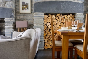 A stone fireplace with stacked wood, a dining table with chairs, and a sofa in a rustic interior. - Garreg Ddu (Blaenau Ffestiniog)
