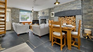 Una sala de estar acogedora con chimenea, paredes de piedra, una mesa de comedor con sillas y un sofá.