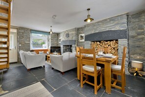 A cozy living room with a fireplace, stone walls, a dining table with chairs, and a sofa. - Garreg Ddu (Blaenau Ffestiniog)