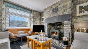 Un salón acogedor con paredes de piedra, una chimenea, un televisor y asientos cómodos.