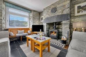 A cozy living room with stone walls, a fireplace, a television, and comfortable seating. - Garreg Ddu (Blaenau Ffestiniog)