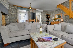 A cozy living room with a sectional sofa, a coffee table with a map, a fireplace, and stone walls. - Garreg Ddu (Blaenau Ffestiniog)