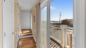 Ein Flur mit Holzboden, weißen Türen und einem großen Schiebeglasfenster, das auf einen Balkon mit weißer Brüstung führt.