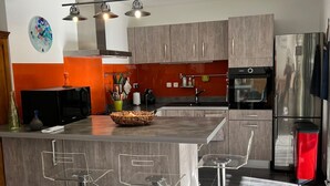 Una cocina moderna con una isla central, taburetes de bar, electrodomésticos de acero inoxidable y un reloj decorativo en la pared.