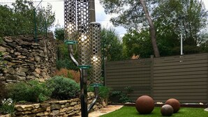Un jardín bien cuidado con césped artificial, un muro de piedra y una escultura de metal.