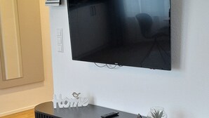 Ein modernes Wohnzimmer mit einem flachbildfernseher an der Wand, einem schwarzen Konsolentisch und einem dekorativen Gegenstand sowie einem Holzboden.