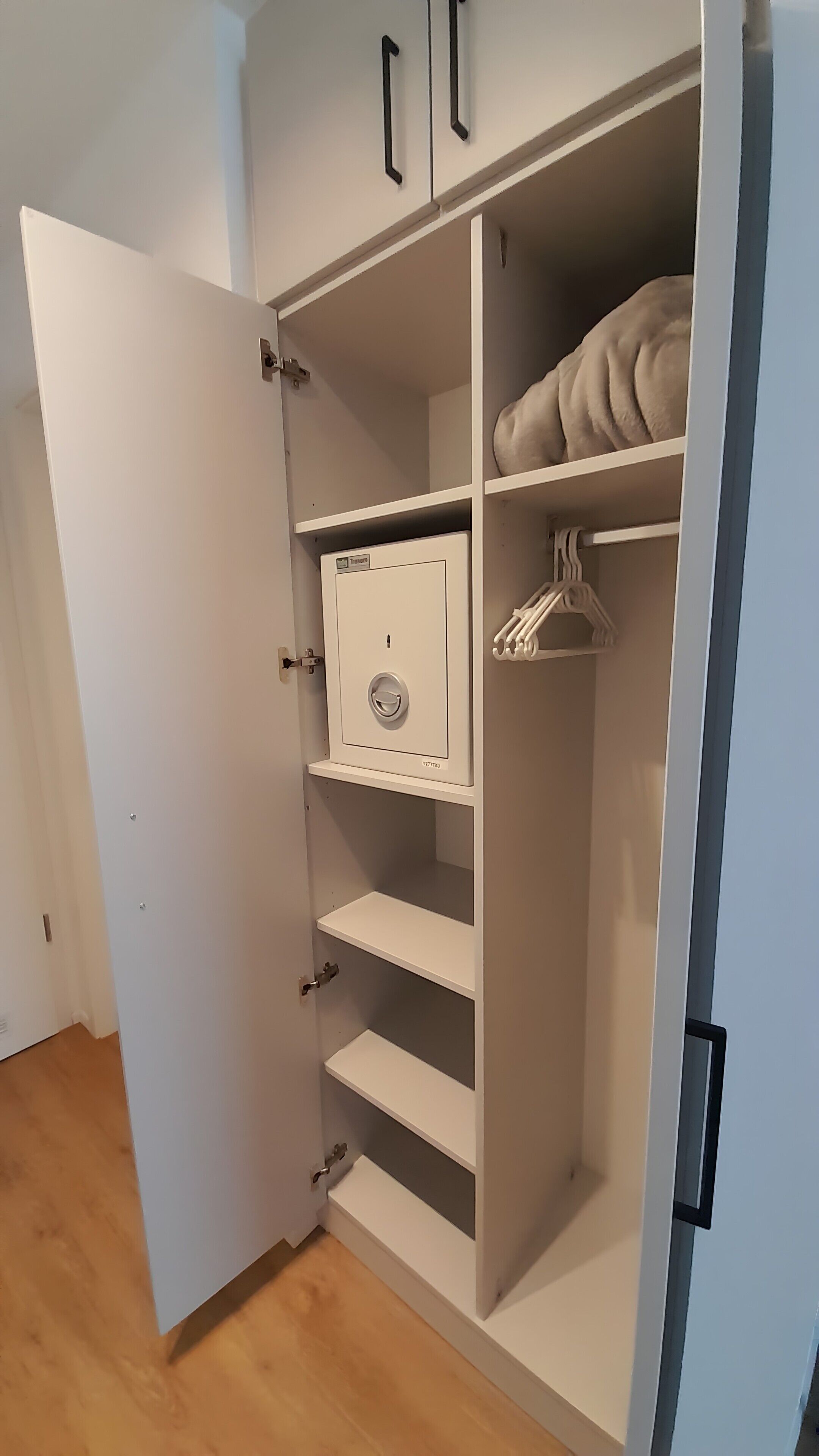 Een witte kast met meerdere planken, een kledingroede en een afsluitbaar kastje.