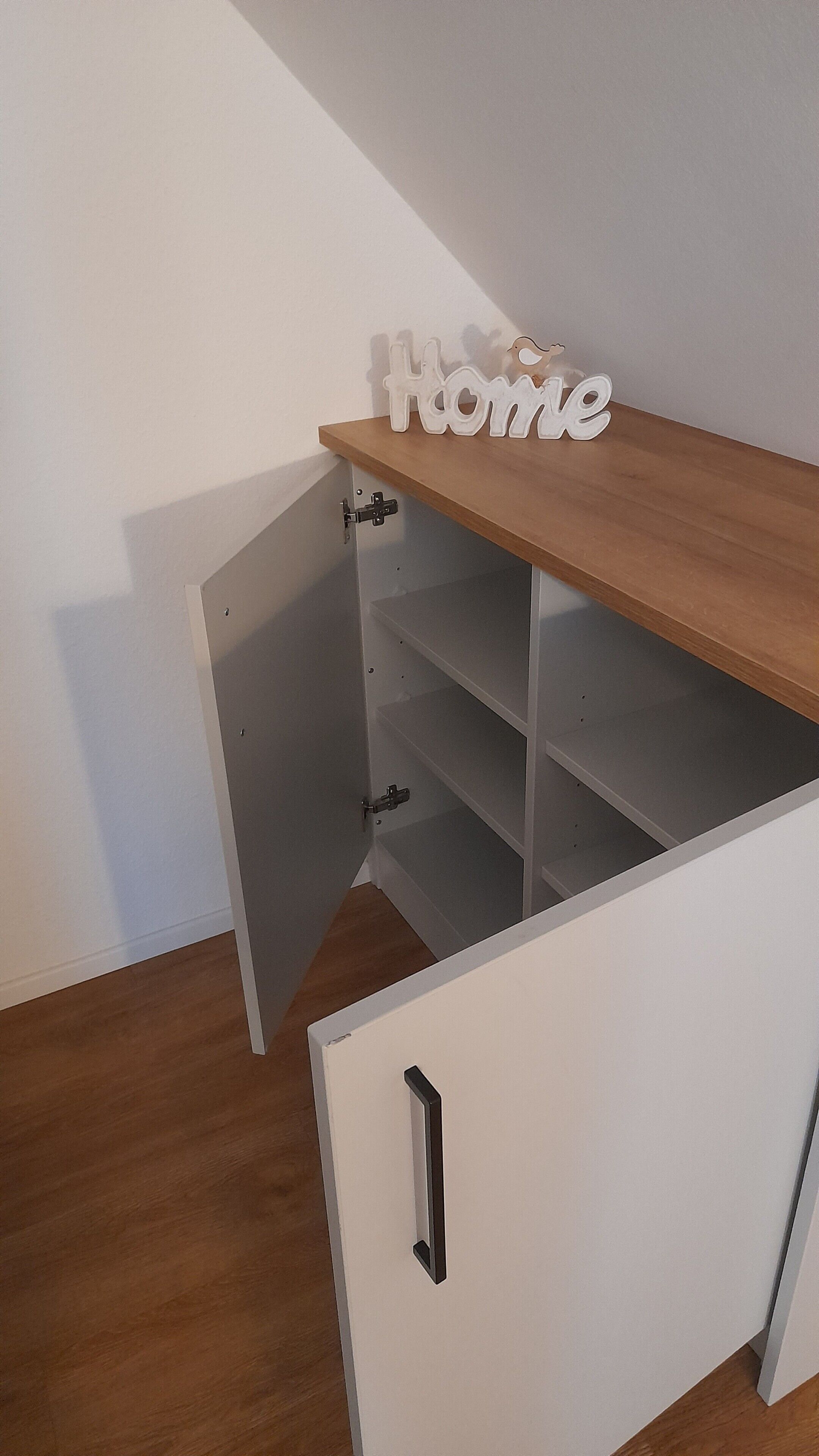 Un meuble blanc avec une étagère supérieure en bois, une enseigne portant le mot «Accueil» et un petit oiseau décoratif.
