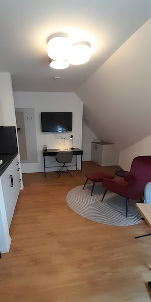 Un salon moderne avec un téléviseur à écran plat, un bureau, un fauteuil rouge et un plancher en bois.