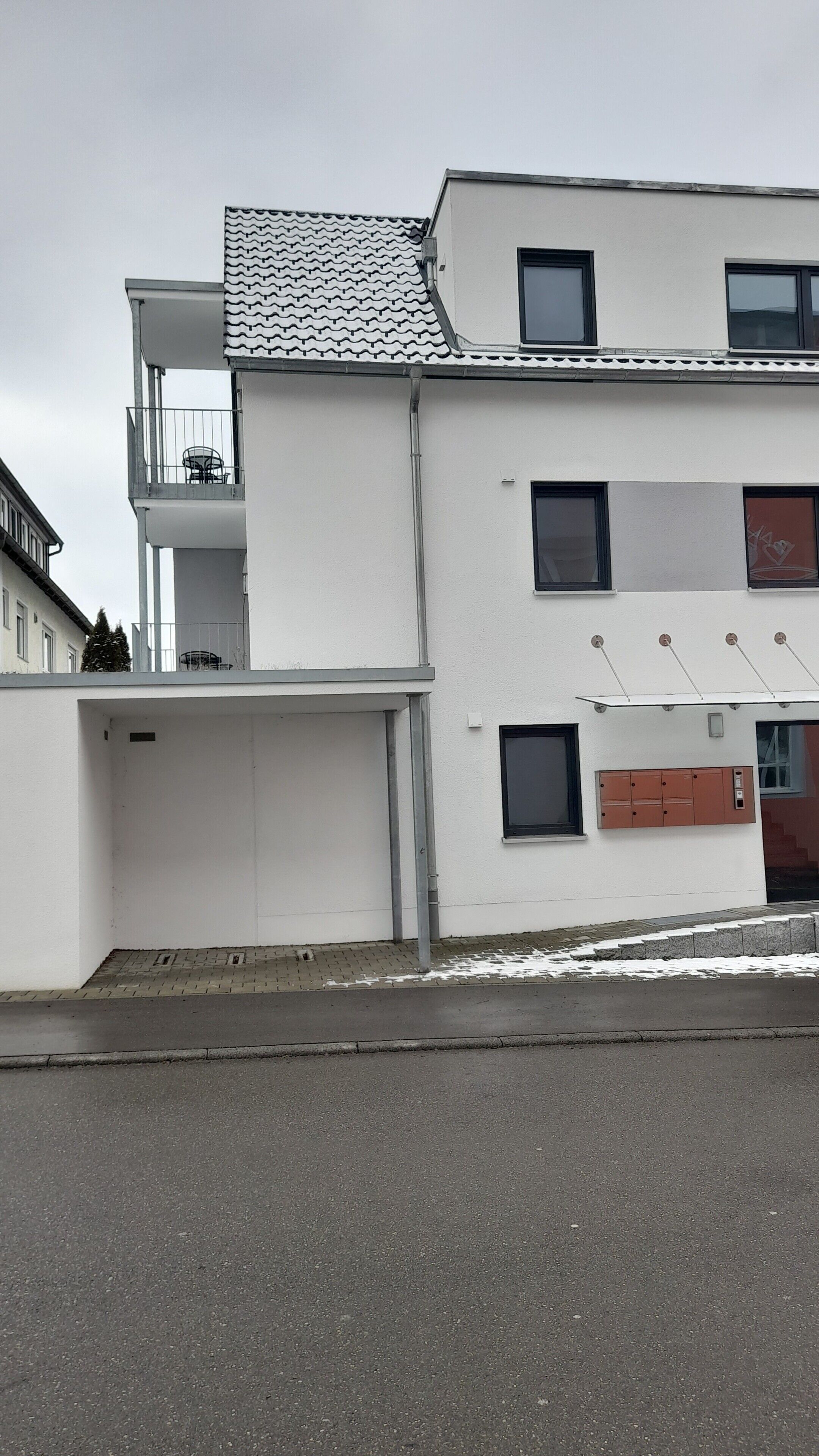 A modern building with a flat roof, multiple windows, and a visible balcony.