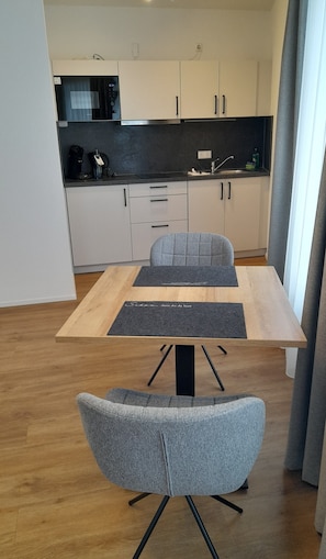 Une cuisine moderne avec des meubles blancs, un plan de travail noir et un coin repas comprenant une table en bois et des chaises à revêtement gris.