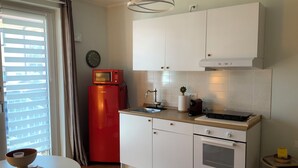 Kompakti keittiö, jossa on valkoiset kaapit, punainen jääkaappi, pesuallas ja pieni työtaso.