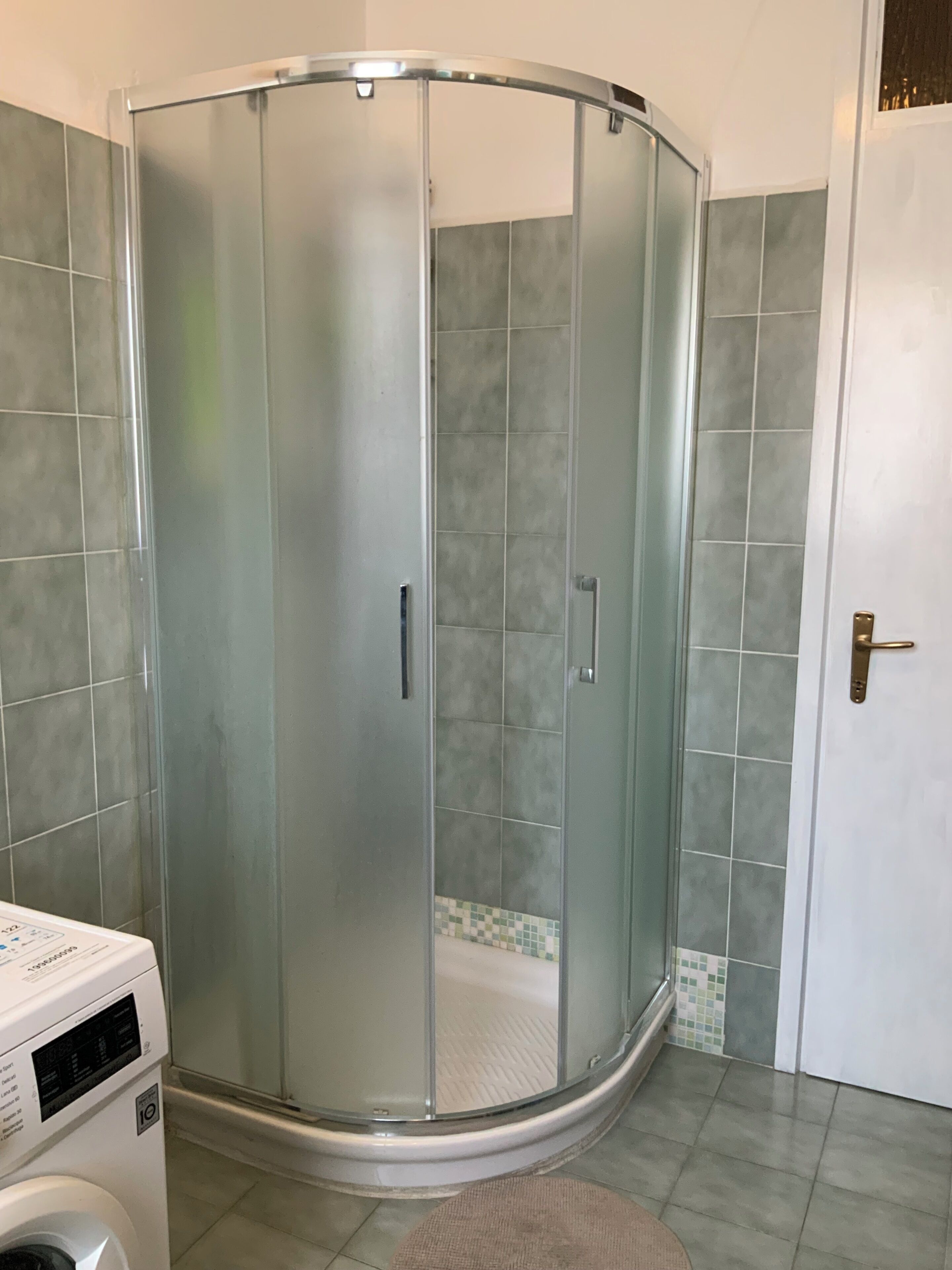 Ducha en esquina con puertas de vidrio, lavadora y paredes con azulejos.