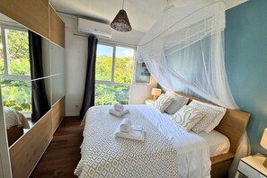 Ein Schlafzimmer mit Bett, Nachttischen, einem Fenster mit Vorhängen, einer Pendelleuchte und einem Moskitonetz.